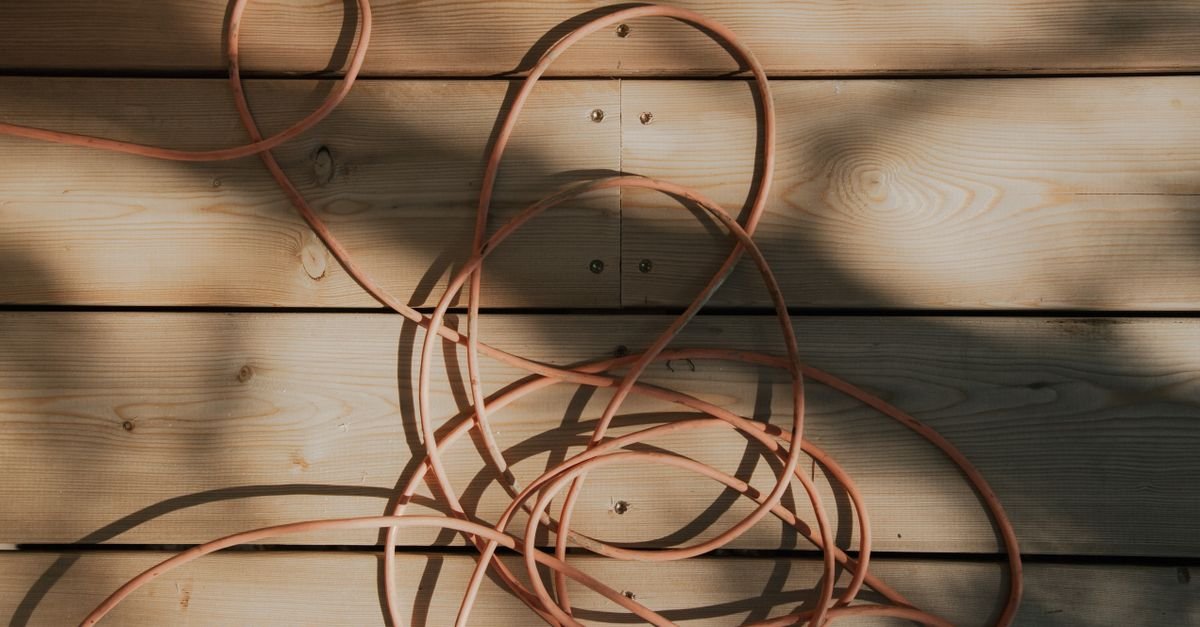 An orange extension cable coiled loosely across sunlit outdoor decking boards