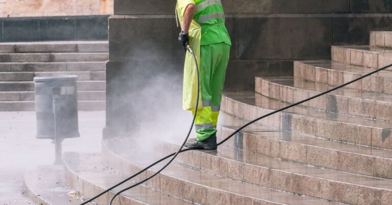 A worker using a pressure washer turbo nozzle to clean weathered stone steps in a public park