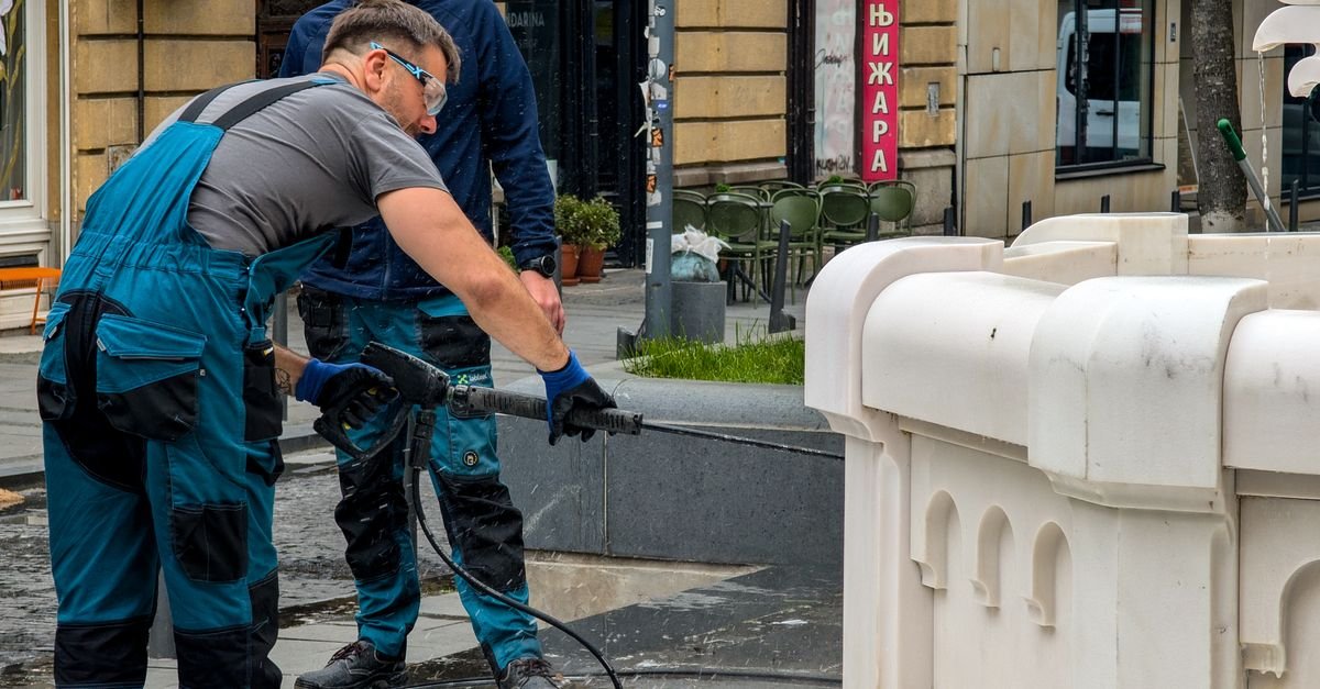 Two workers clearing heavy grime from a stone fountain with high-pressure spray