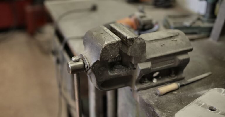 A bench vise mounted on a workbench surrounded by hand tools, photographed from above