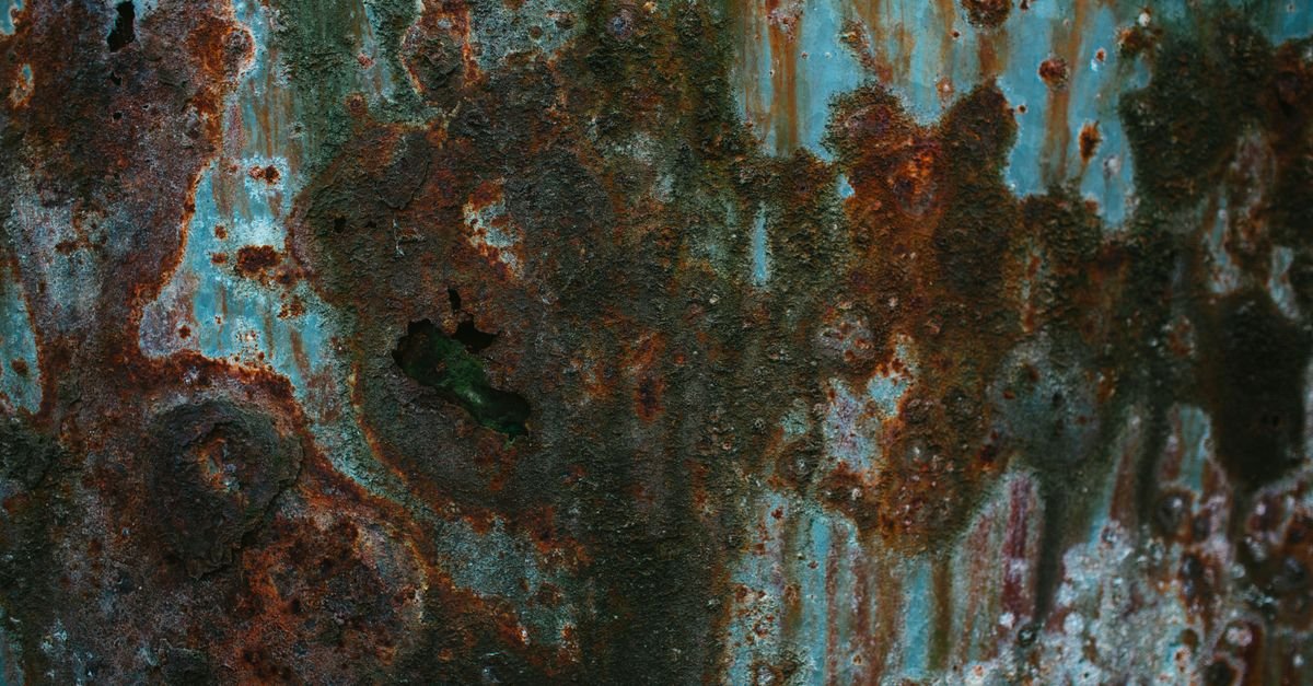 Metal surface visibly eroded by moving water, the same slow mechanism that widens a nozzle orifice over hundreds of hours