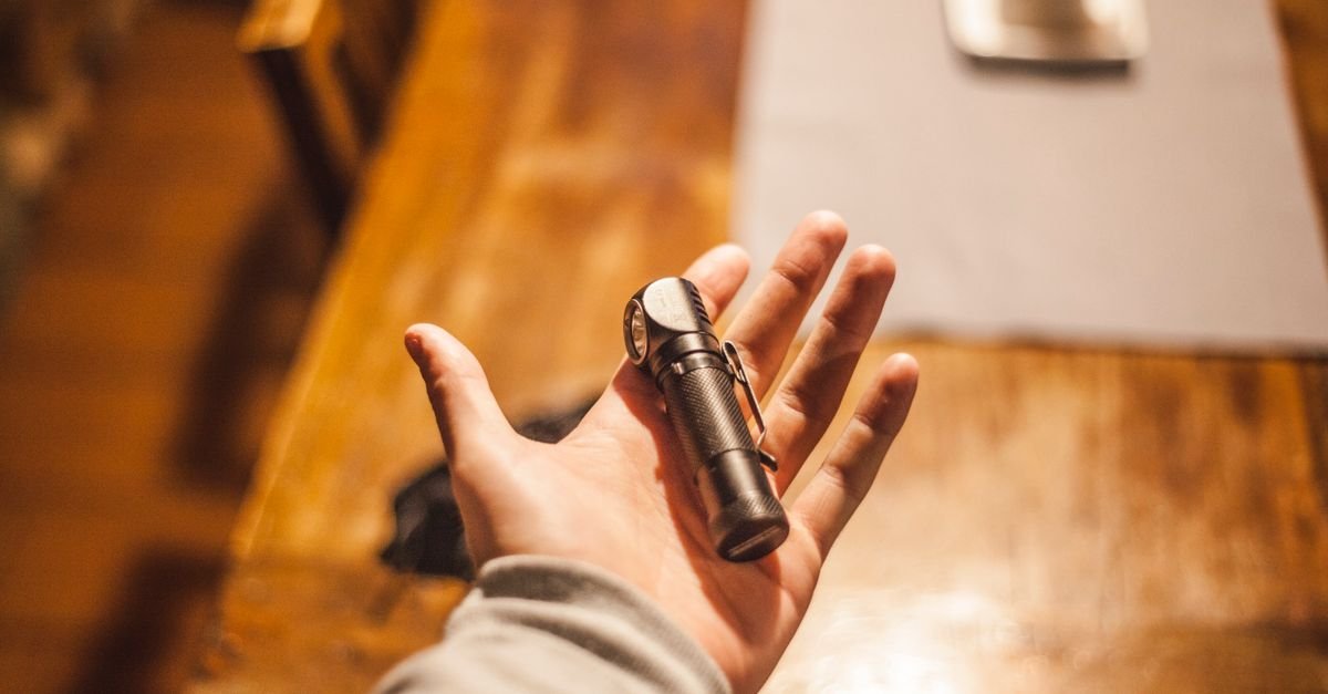 A hand holding a small flashlight on a workbench, the tool that turns a nozzle orifice into something you can actually inspect