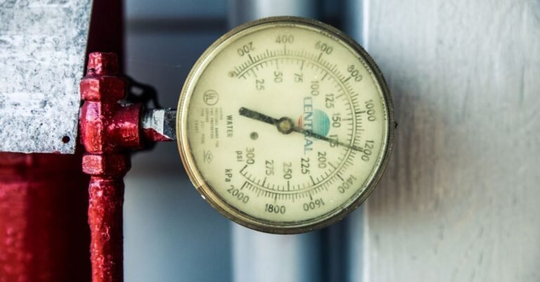 A pressure gauge mounted on a red industrial pipe showing both PSI and kPa scales