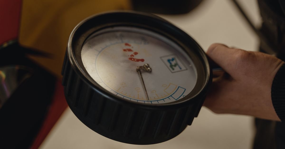 A hand holding a pressure gauge in a mechanical workshop setting