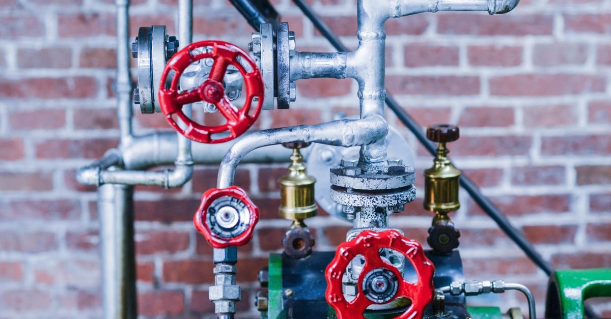 Industrial machinery with red valve handles and steel pipework against a brick wall