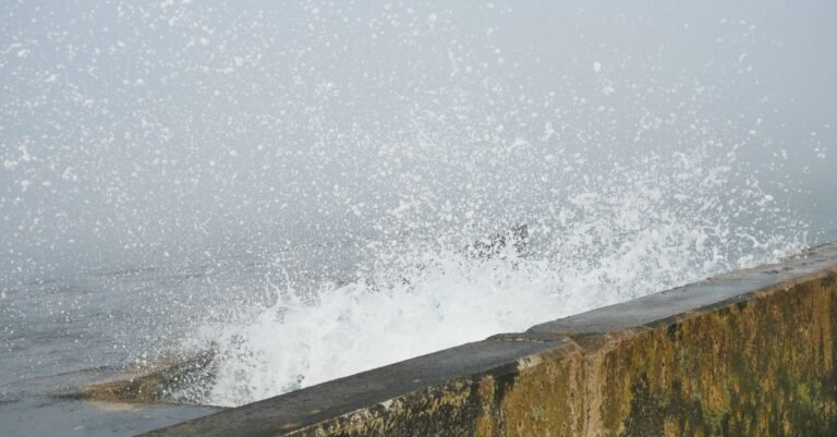 Ocean waves crashing into a weathered concrete seawall and throwing spray upward, moving water brought to a dead stop by something solid