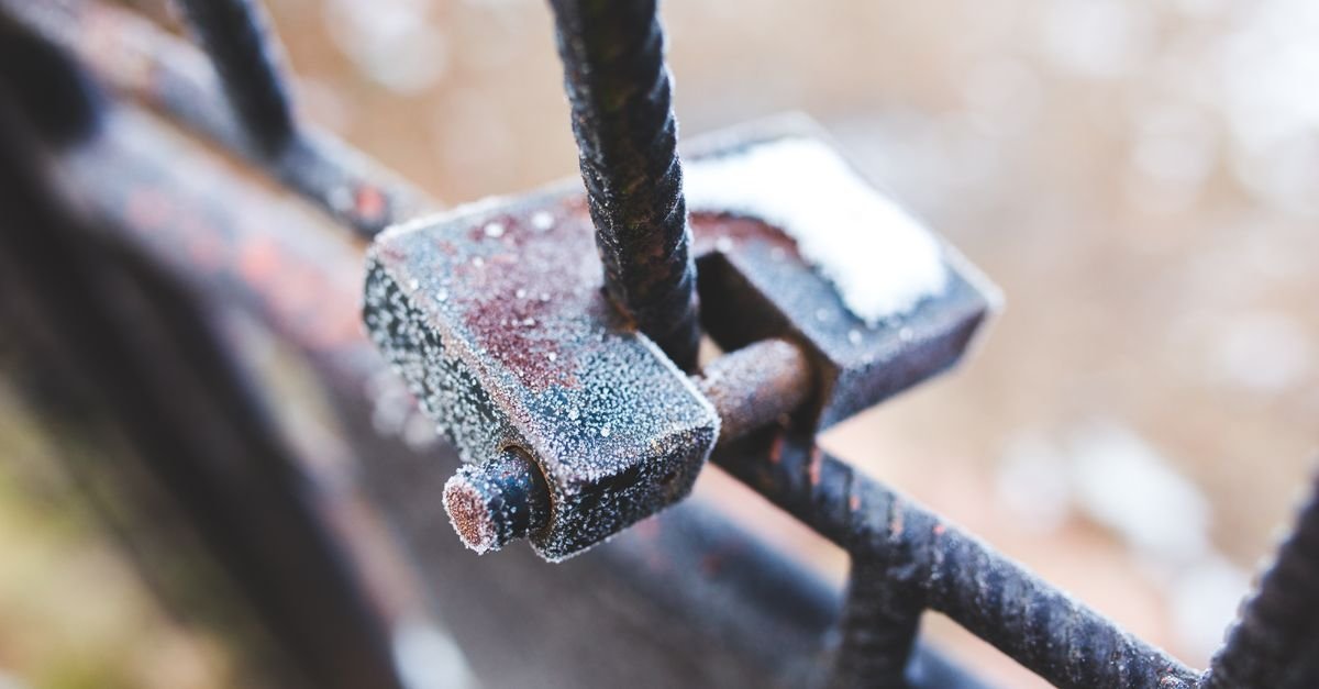 A frost-covered rusted padlock on an iron fence in winter, the damage a cold garage does slowly