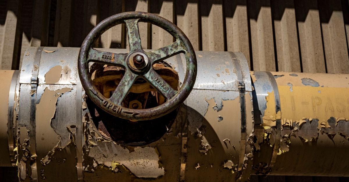A corroded valve body on a weathered pipe, the kind of one-way valve that stops sealing once grit gets under it
