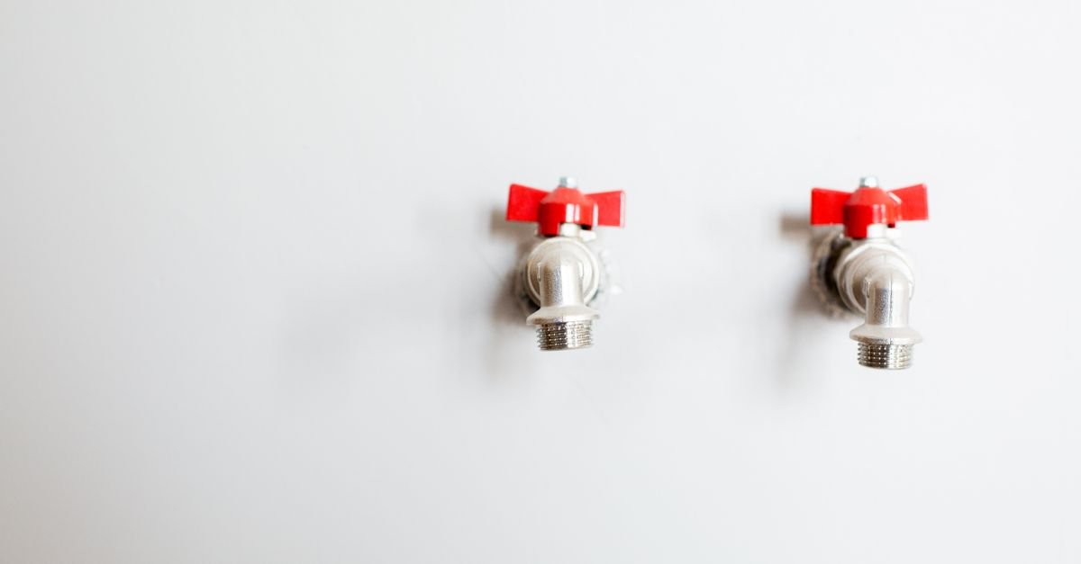 Two outdoor taps with red handles on a wall, the supply that has to be fully open before a pump can prime