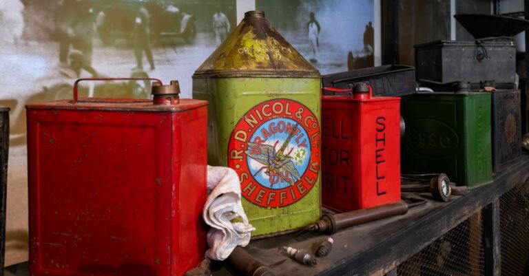 Old metal fuel and oil cans lined up on a wooden garage shelf, the leftover fuel that ruins a spring start