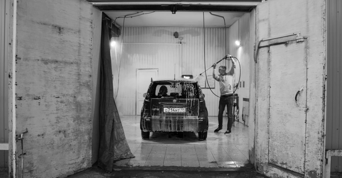 A person washing a car with a pressure washer inside a garage, the motor running steadily between passes