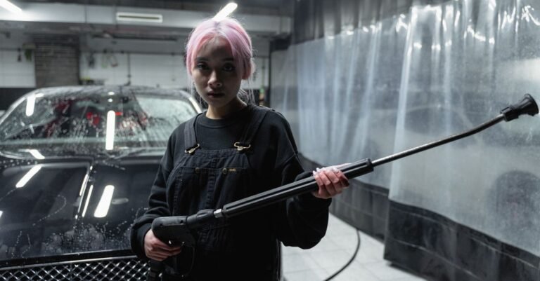 A person gripping a live pressure washer trigger gun while rinsing a car, the machine still running behind them