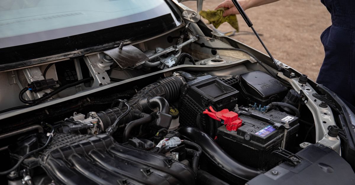 Mechanic leaning over an open engine bay inspecting the car battery and terminals during routine maintenance