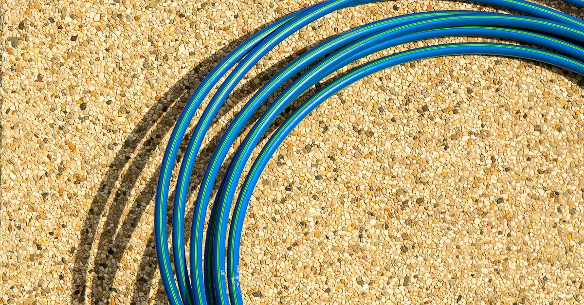 Close-up of a blue hose coiled on a textured concrete surface in sunlight