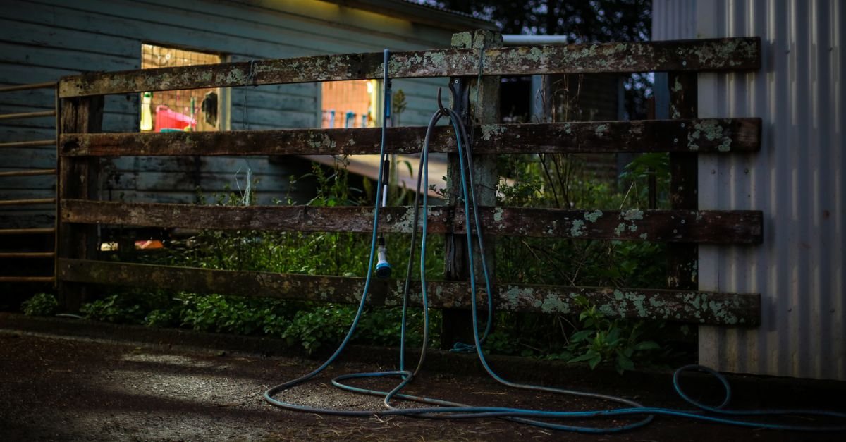 Garden hose hanging on a weathered wooden fence at dusk