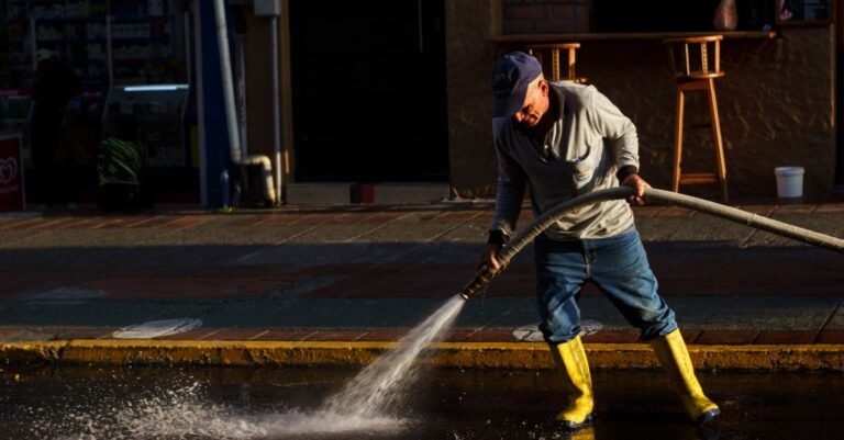 Worker in yellow boots dragging a long high-pressure hose while cleaning a city street