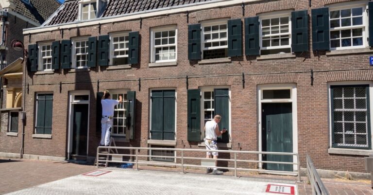 Two painters on a ladder and scaffold preparing the facade of a brick house on a sunny day