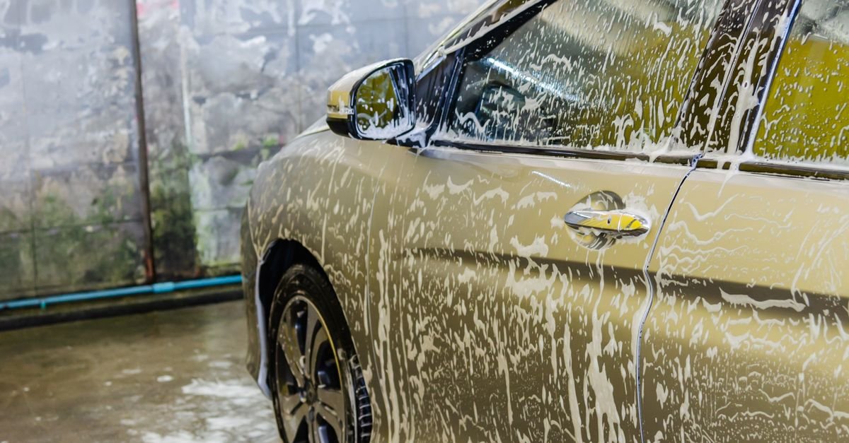 Car covered in a thick blanket of white soap foam at a wash bay