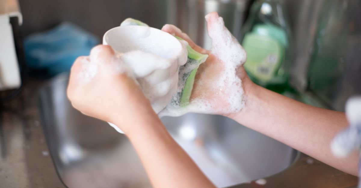 Hands washing a cup with dish soap suds in a kitchen sink