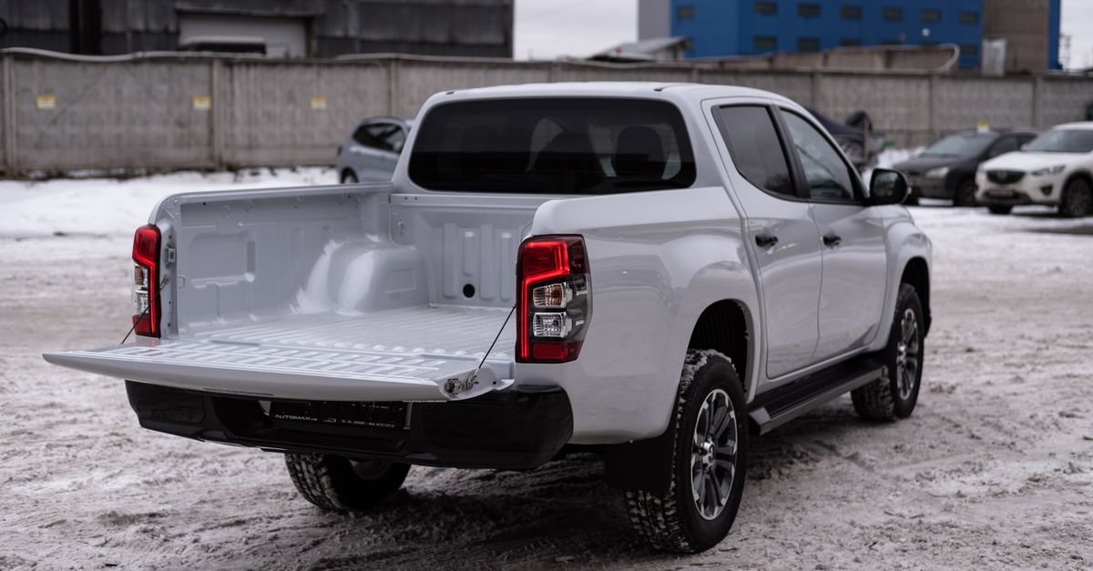 A white pickup truck with an open cargo bed parked in a snowy industrial yard