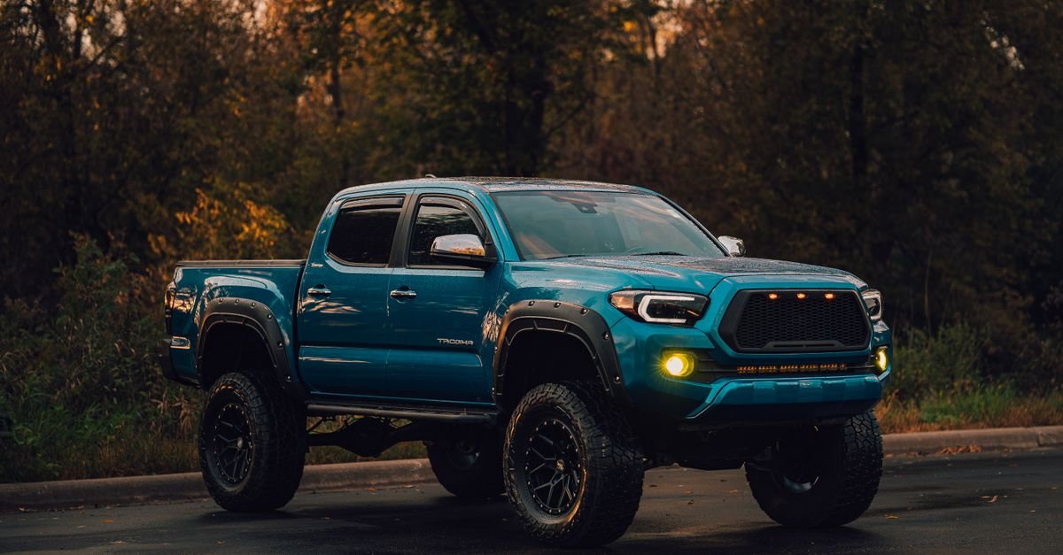 A lifted blue pickup truck parked on a wet forest road