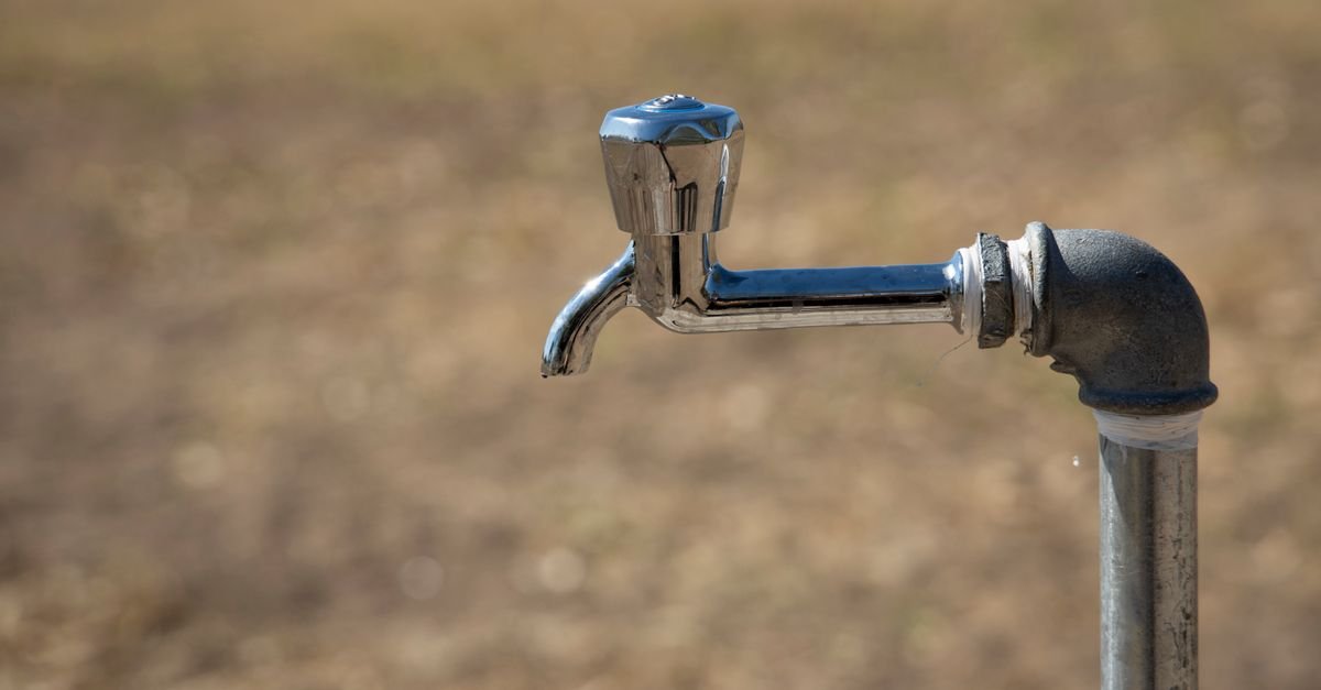 Weathered outdoor metal faucet on an exterior wall, the supply point that usually turns out to be too slow
