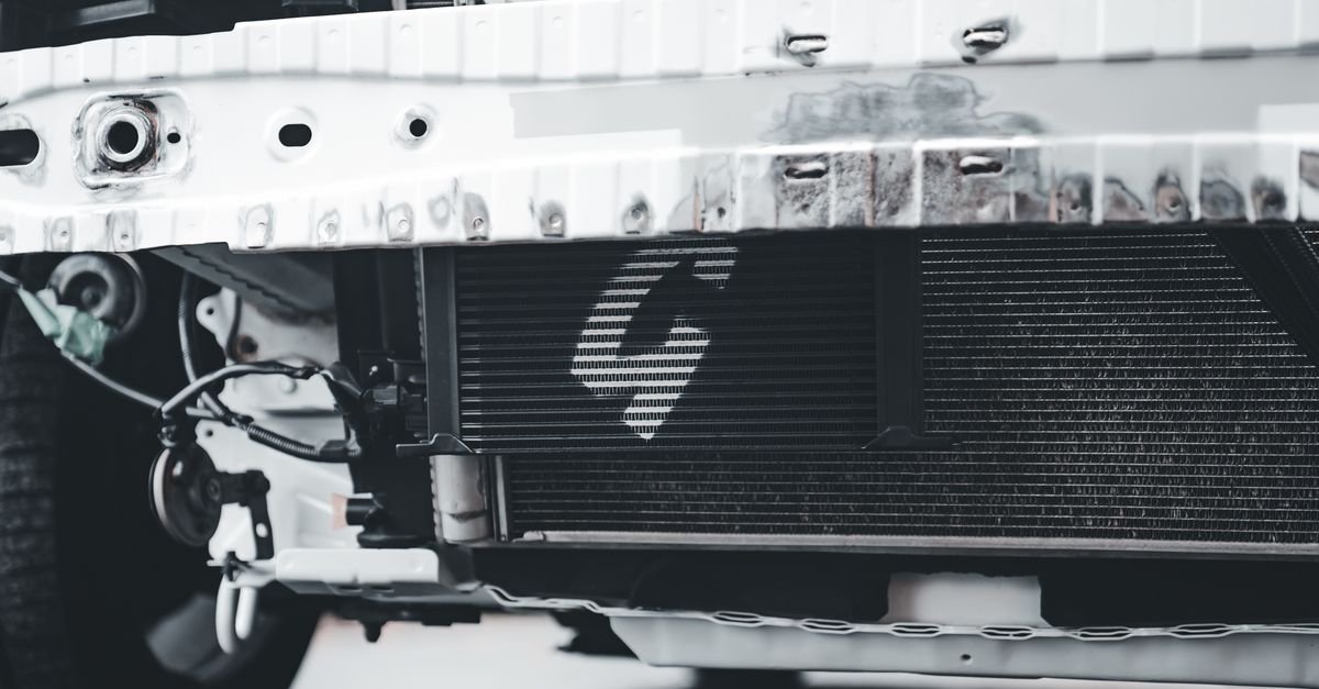 Close-up of a car radiator behind the front bumper, showing the fins and tanks the coolant circulates through