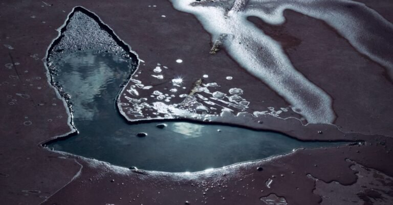 A shallow puddle of standing water spread across a bare concrete slab, reflecting the sky above it