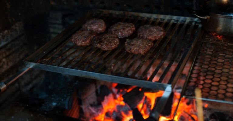 Burger patties on a barbecue grate seen from above with flames rising through the bars