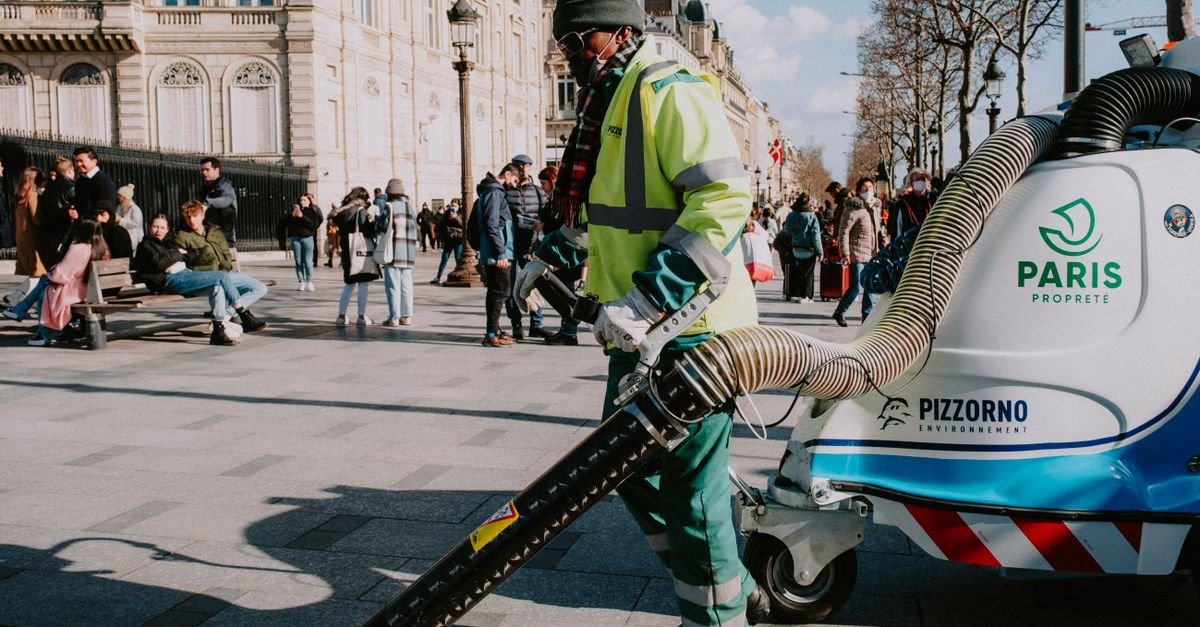 A street cleaning operative in high-visibility clothing working equipment along a Paris pavement
