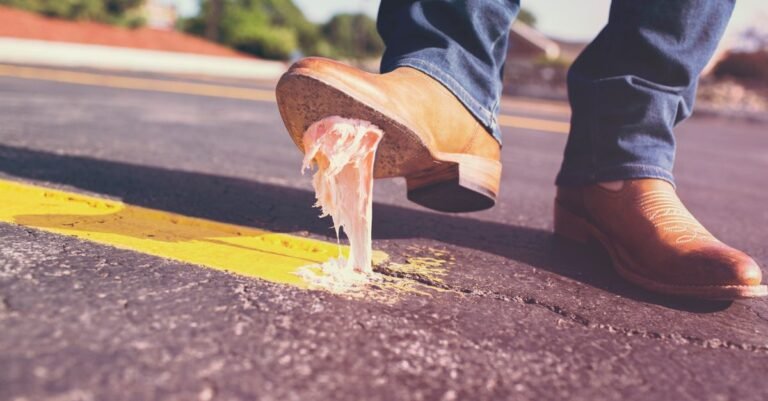 Close-up of a shoe pressing down on a flattened piece of chewing gum stuck to a city street