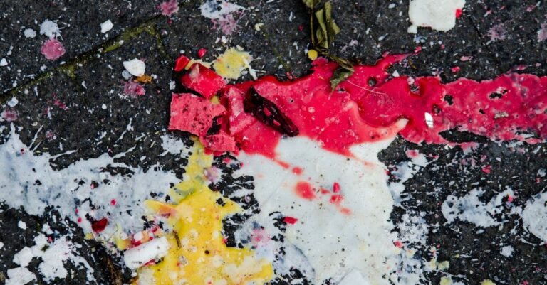 Fine coloured paint droplets scattered across a section of grey urban pavement