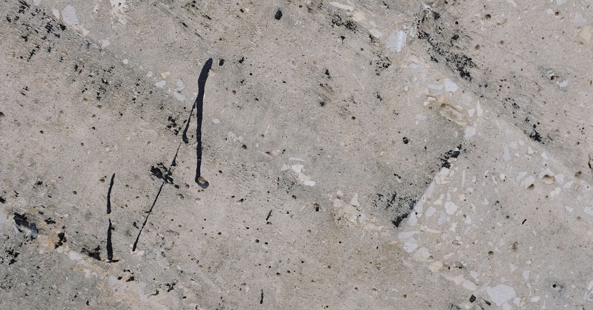 Close-up of a rough textured concrete surface carrying dried black paint spatter