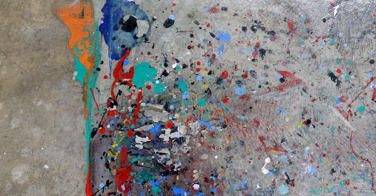 Fine paint spatter in several colours drying across a rough grey concrete surface