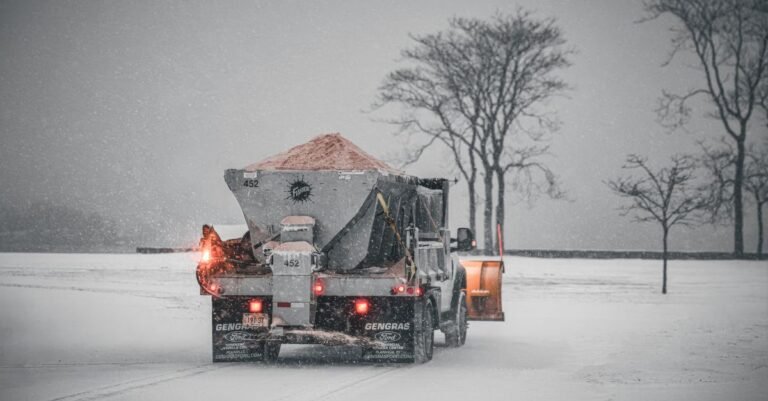 Snowplough truck spreading de-icing salt along a snow-covered road during a winter storm