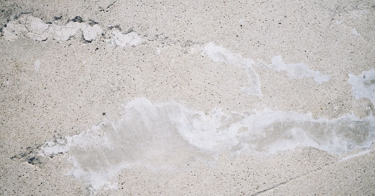 Overhead view of a rough concrete surface with cracks and loose sandy grit across it
