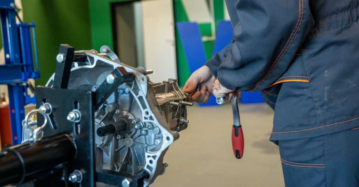 A car gearbox clamped to a workshop stand while a technician works on the casing