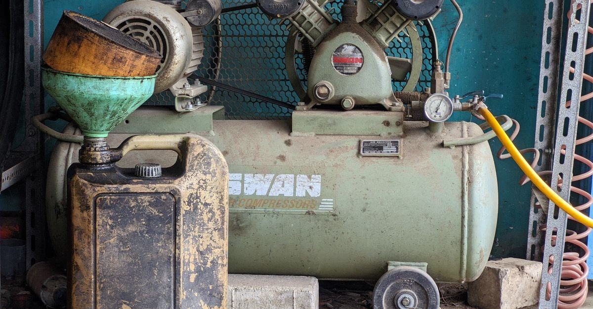 An old compressor and an oil can sitting in a dusty workshop corner