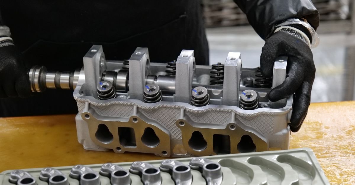 A technician assembling a cylinder head with precision components laid out on a workbench in order
