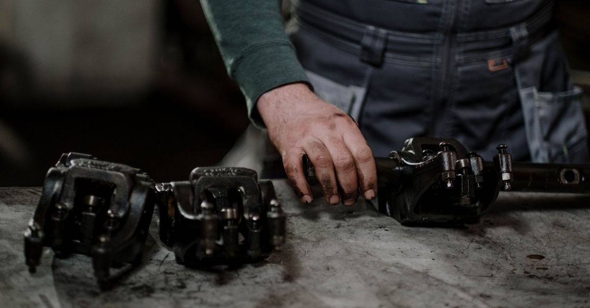 A mechanic handling greasy metal components on a workbench, inspecting worn parts before ordering a repair kit