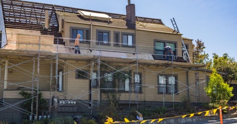 A house under renovation with scaffolding erected to the eaves and workers on the roof
