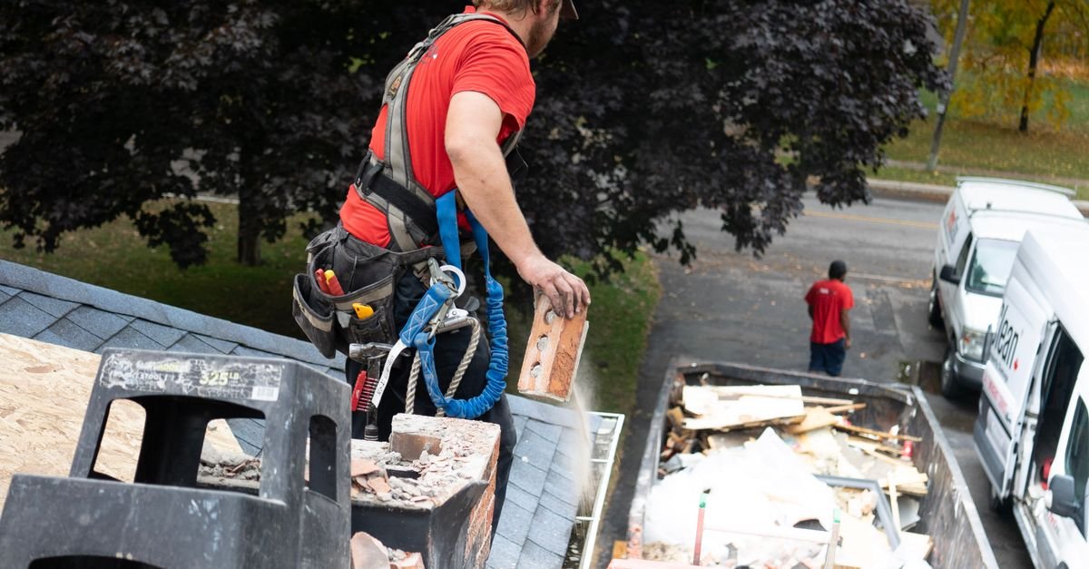 A worker in a full-body safety harness working at the edge of a roof