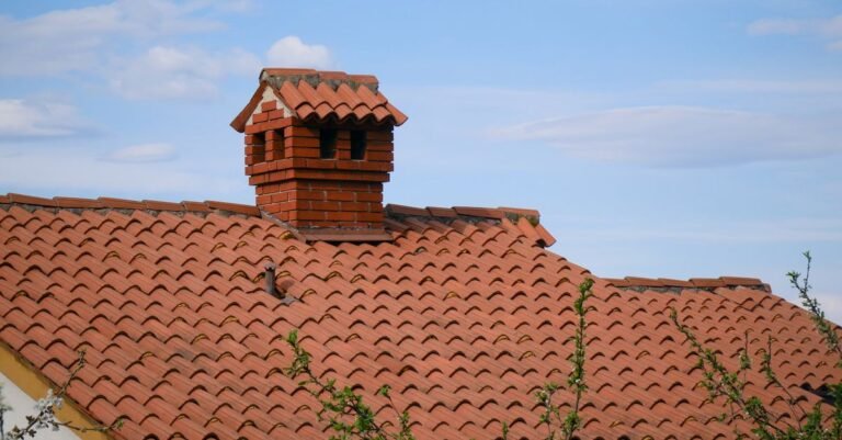 Red brick chimney rising from a clay tile roof, the lapped tile courses visible below it