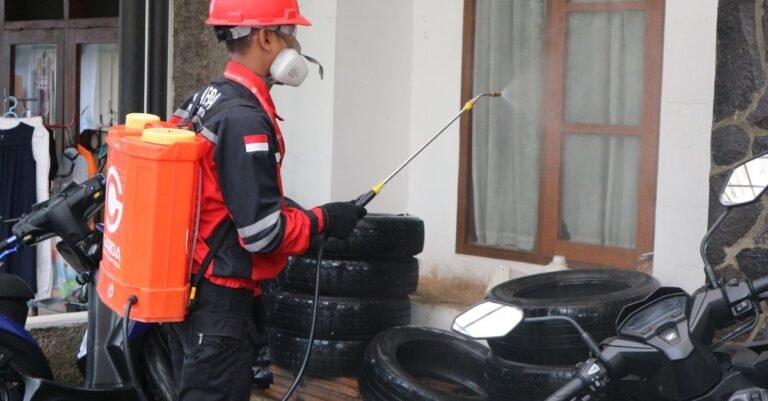 A worker in protective gear spraying cleaning solution along the outside wall of a building