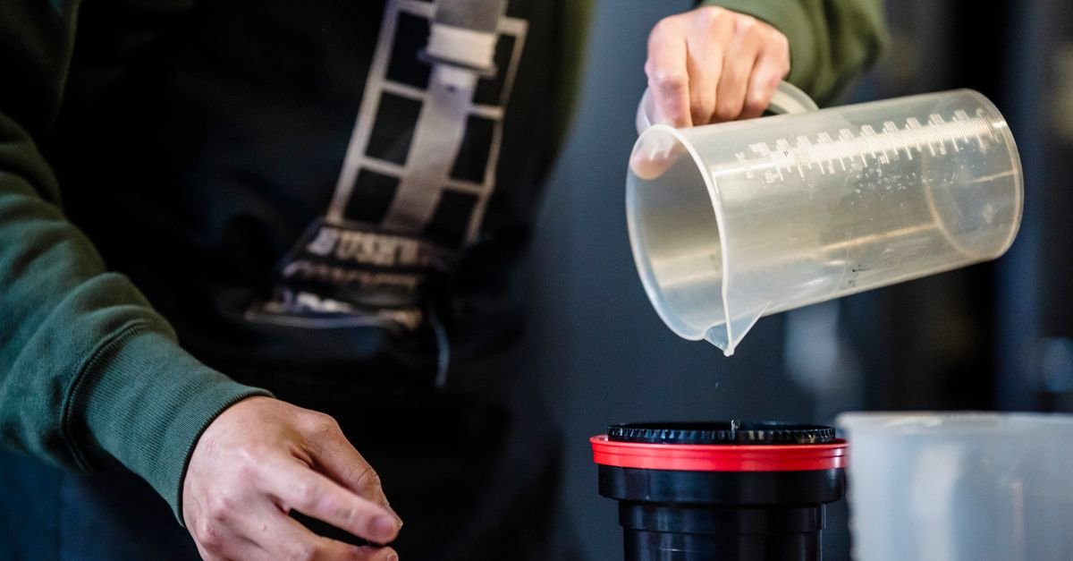 Hands pouring liquid from a graduated measuring cup into a container to make up a cleaning mix