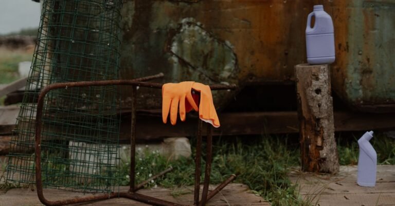 Orange latex gloves and cleaning bottles set out on a wooden deck beside a rusted metal chair