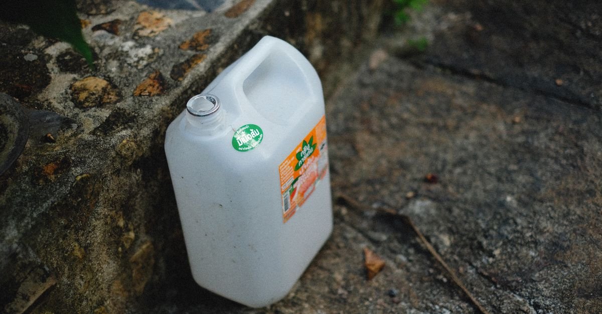 A large white plastic chemical jug standing on a stone surface outdoors