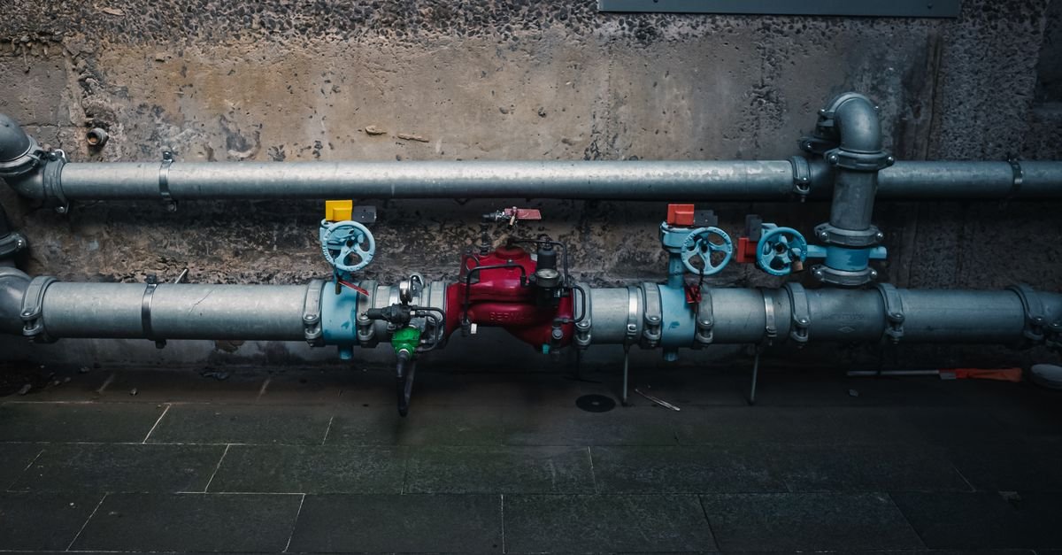 A row of coloured shut-off valves on pipework running along a textured wall