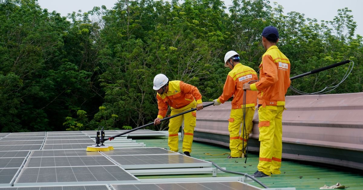 Three technicians in high-visibility uniforms and hard hats working across a rooftop solar array from the walkway beside it