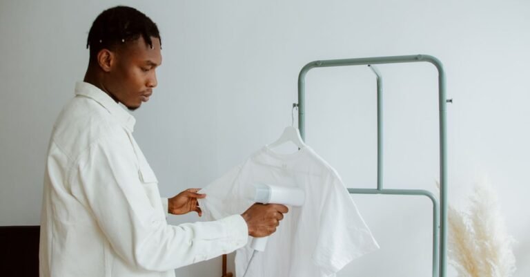 A man holding a handheld garment steamer against a white shirt hanging on a rack in a plain indoor room